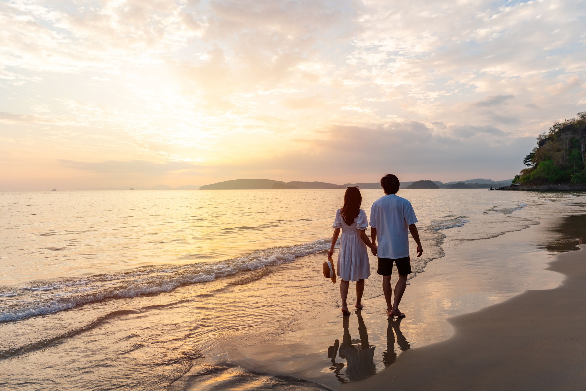Young happiness Asian couple traveler relaxing and watching beautiful Sunset on the tranquil beach, Traveling on summer vacation concept